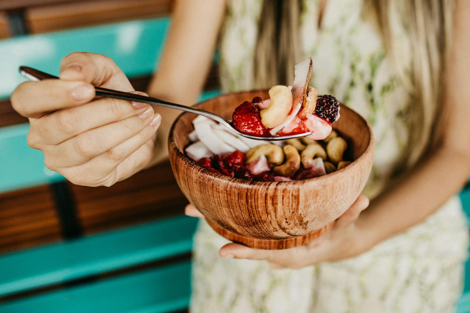 person holding stainless steel spoon with sliced strawberries