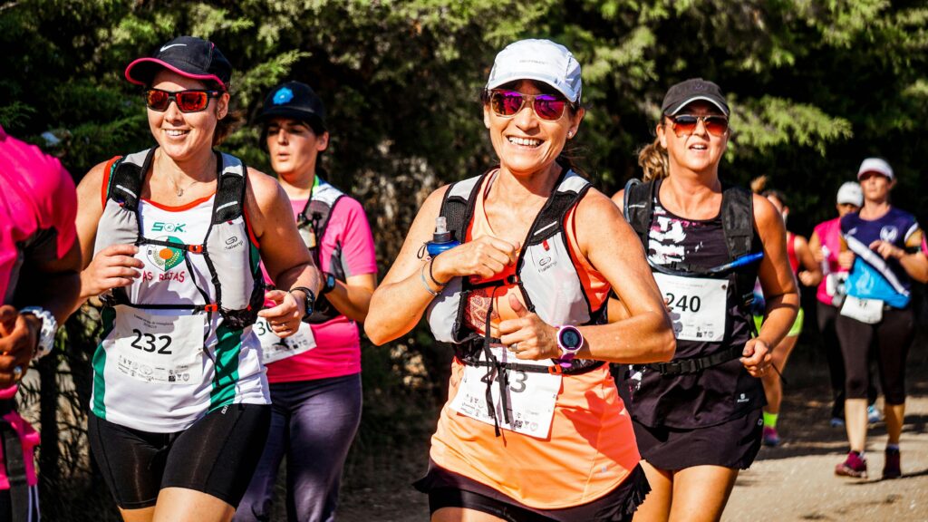 A group of smiling women participating in an outdoor marathon run with race numbers.