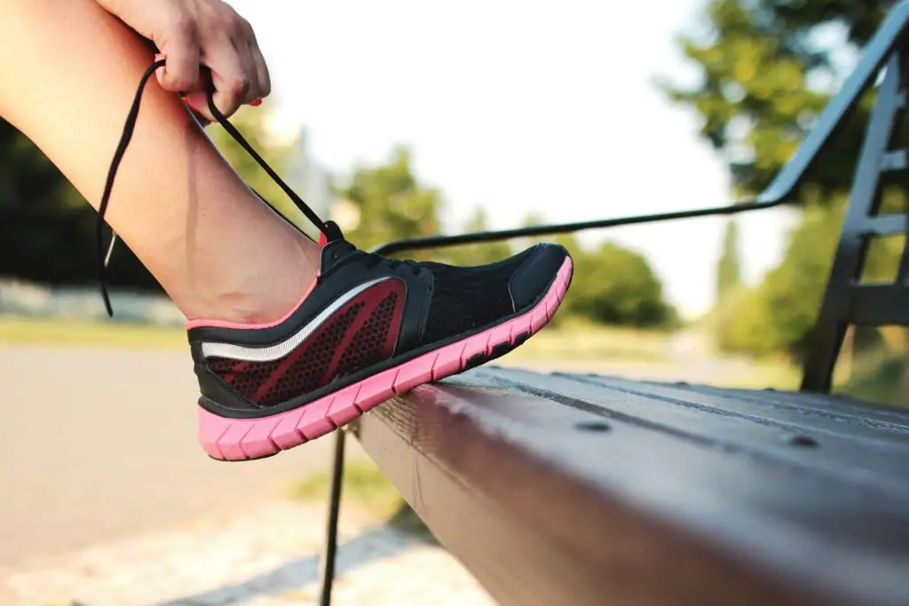 A woman laces her sneakers on a park bench, preparing for a run outdoors.